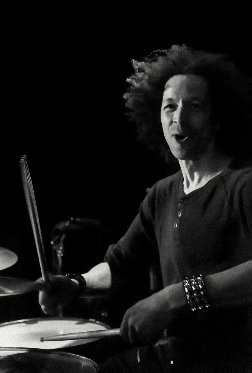 Black and white action shot of Zack smiling while he plays drums.